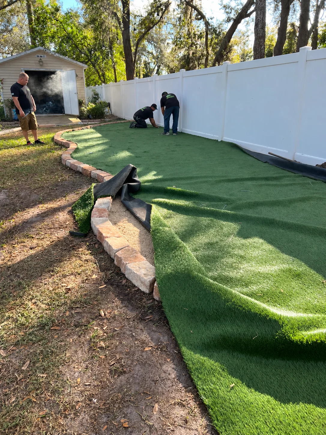 Installers position artificial turf beside the curved stone border