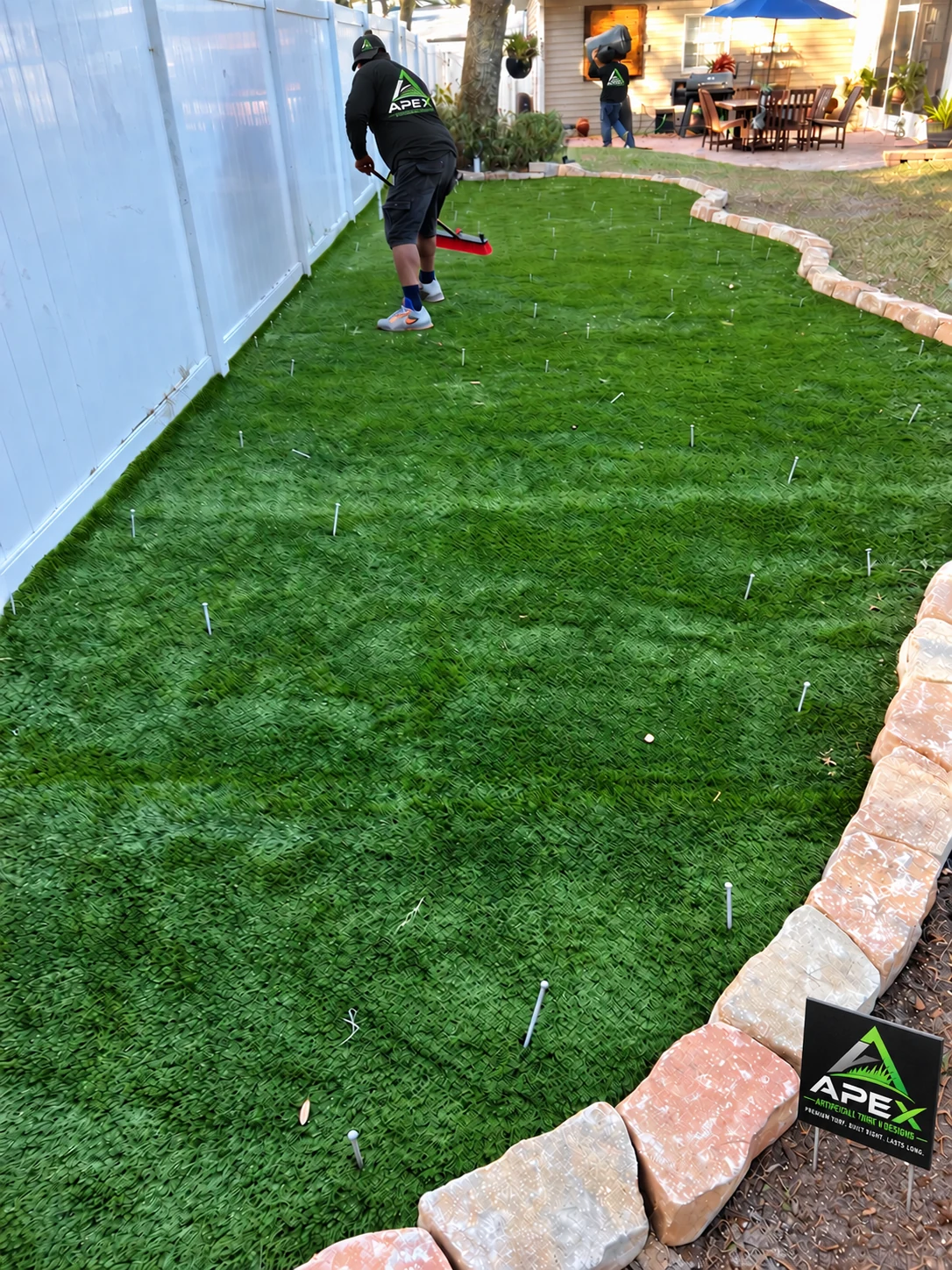 Worker grooms newly installed turf along the white fence