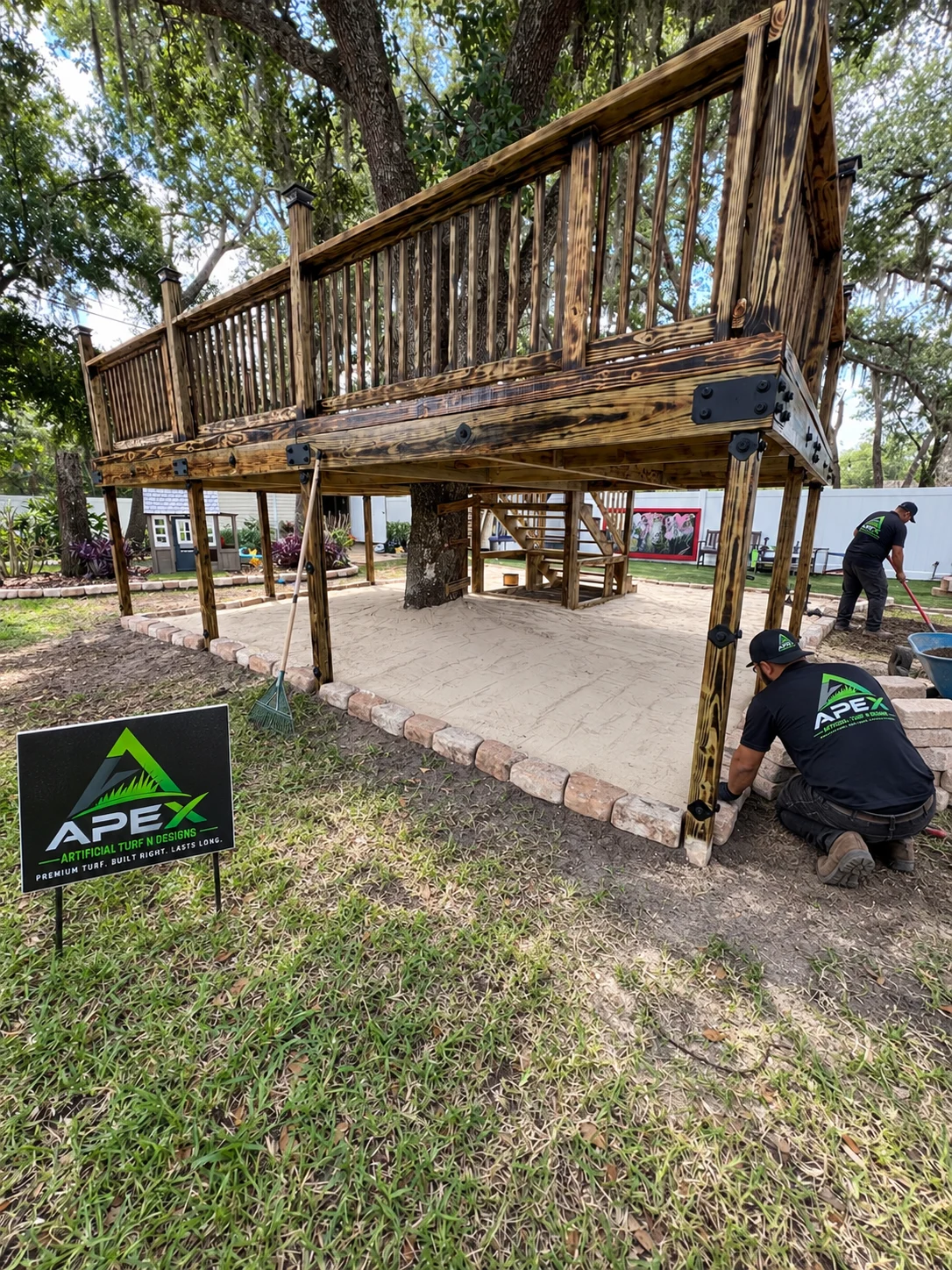 Apex crew preparing the turf area around a raised wooden deck with an Apex yard sign