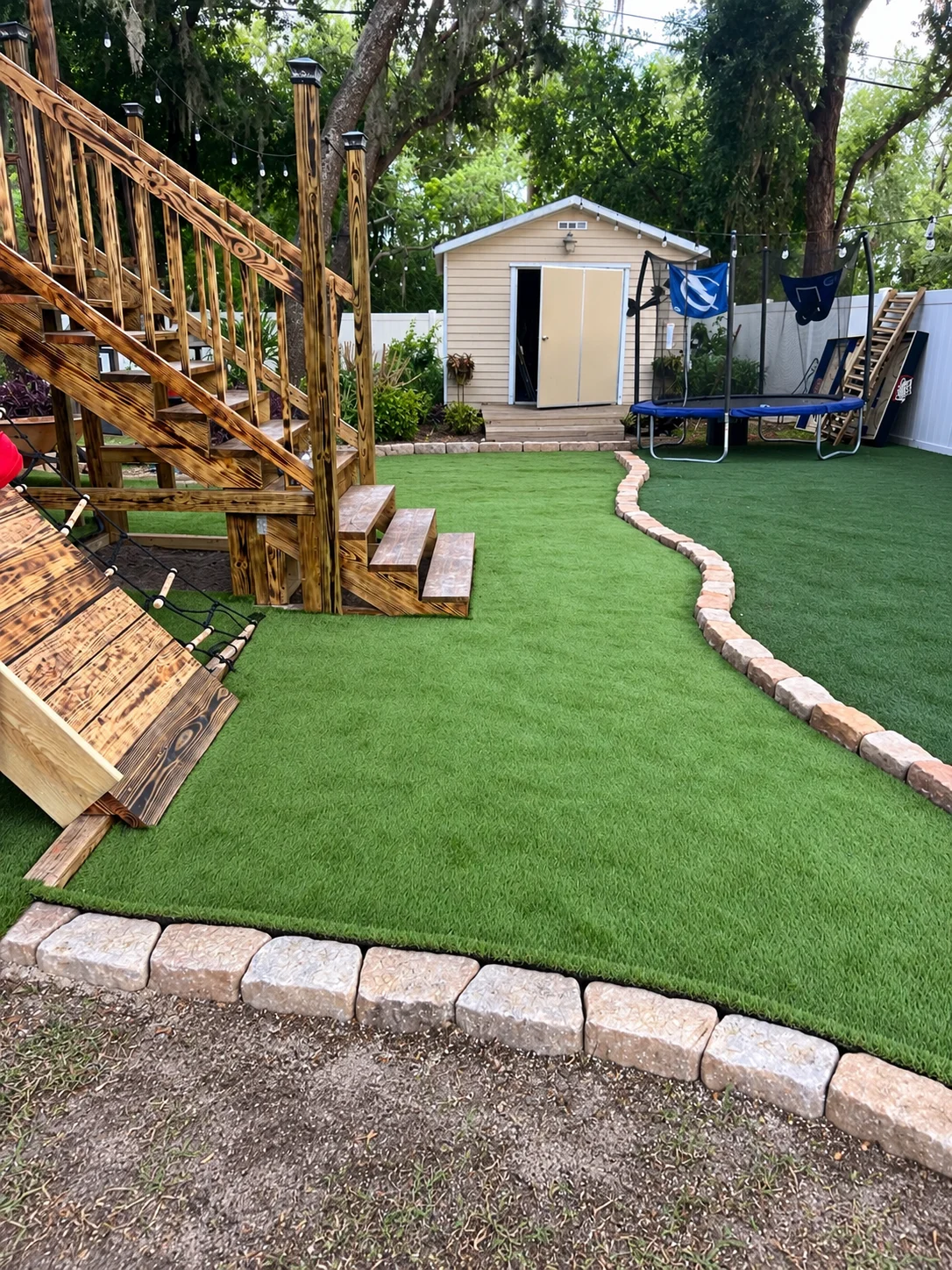 Artificial turf installation beside the curved stone border and raised play structure
